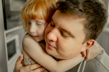 Mann mit geschlossenen Augen umarmt Tochter zu Hause - ANAF00710