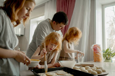 Junge Eltern bereiten mit ihren Töchtern zu Hause Käsekuchen zu - ANAF00720