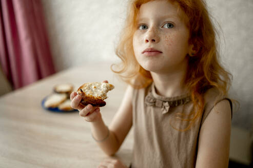 Rothaariges Mädchen isst Käsekuchen am Tisch - ANAF00728