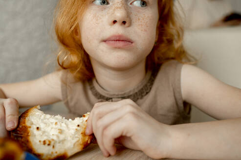 Mädchen mit Sommersprossen im Gesicht isst Käsekuchen zu Hause - ANAF00729