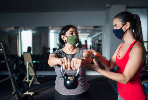 Aktive ältere Frau mit Personal Trainer macht Übungen im Fitnessstudio, Coronavirus Konzept. - HPIF05156