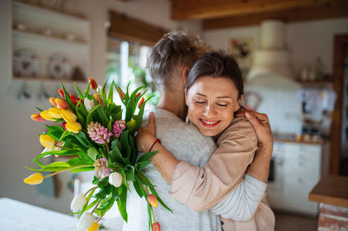 Eine glückliche ältere Mutter umarmt erwachsene Tochter drinnen zu Hause, Muttertag oder Geburtstagsfeier. - HPIF05167