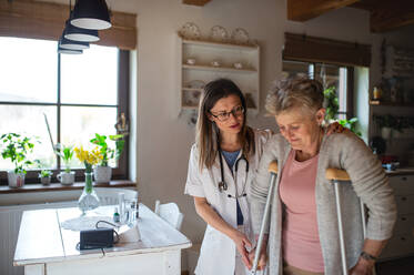 A healthcare worker or caregiver visiting senior woman indoors at home, helping her to walk. - HPIF05210