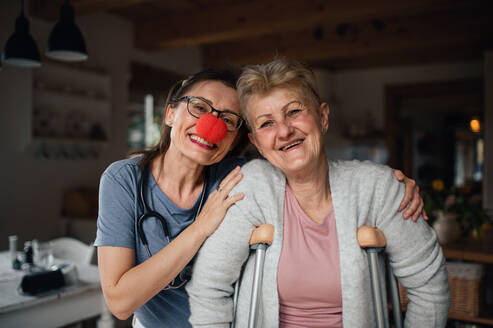 Eine Pflegekraft mit roter Nase besucht eine ältere Frau zu Hause und schaut in die Kamera. - HPIF05230