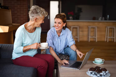 A happy senior mother having coffee with adult daughter indoors at home, sitting, talking and using tablet. - HPIF05254