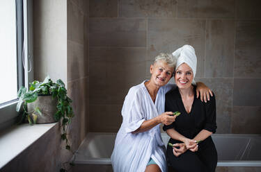 A happy senior mother in bathrobe with adult daughter indoors at home, selfcare concept. - HPIF05266