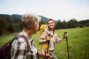 Eine glückliche erwachsene Frau mit Trekkingstöcken, die mit einer aktiven älteren Mutter draußen in der Natur wandert. - HPIF05267