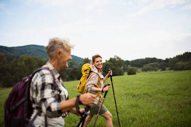 Eine glückliche erwachsene Frau mit Trekkingstöcken, die mit einer aktiven älteren Mutter draußen in der Natur wandert. - HPIF05269