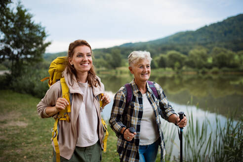 Eine glückliche ältere Frau mit Trekkingstöcken, die mit ihrer erwachsenen Tochter draußen in der Natur wandert. - HPIF05283