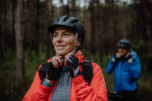 Ein älteres Paar Radfahrer setzen auf Fahrradhelm im Freien im Wald im Herbst Tag. - HPIF05289