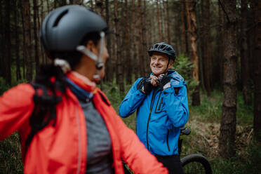 Ein älteres Paar Radfahrer setzen auf Fahrradhelm im Freien im Wald im Herbst Tag. - HPIF05290