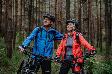 Ein älteres Radlerpaar mit E-Bikes bewundert die Natur im Wald an einem Herbsttag. - HPIF05294