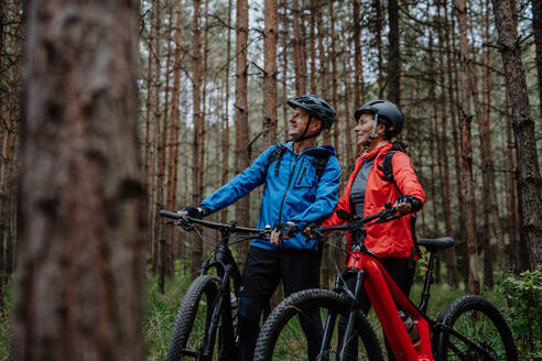 Ein älteres Radlerpaar mit E-Bikes bewundert die Natur im Wald an einem Herbsttag. - HPIF05295