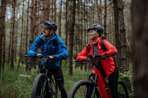 Ein älteres Radlerpaar mit E-Bikes bewundert die Natur im Wald an einem Herbsttag. - HPIF05296