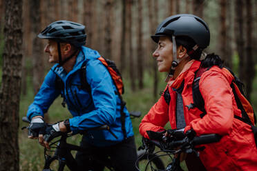 Ein älteres Radlerpaar mit E-Bikes bewundert die Natur im Wald an einem Herbsttag. - HPIF05297