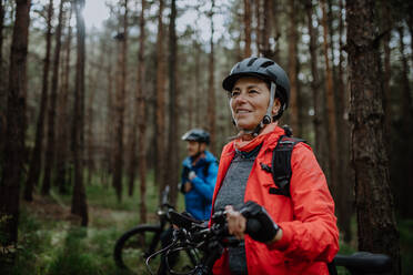 Ein älteres Radlerpaar mit E-Bikes bewundert die Natur im Wald an einem Herbsttag. - HPIF05298