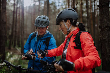 Ein älteres Paar Radfahrer Einstellung Smartwatch im Freien im Wald im Herbst Tag. - HPIF05300