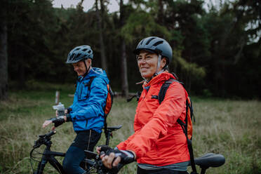 Ein älteres Radlerpaar mit E-Bikes bewundert die Natur im Wald an einem Herbsttag. - HPIF05305