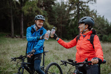 Ein glückliches älteres Paar Radfahrer mit Wasserflaschen im Freien im Wald im Herbst Tag. - HPIF05307