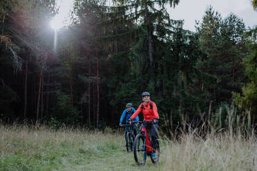 An active senior couple riding bikes outdoors in forest in autumn day. - HPIF05308