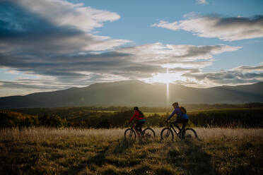 Ein aktives Seniorenpaar fährt in der Abenddämmerung in der herbstlichen Natur Fahrrad. - HPIF05320