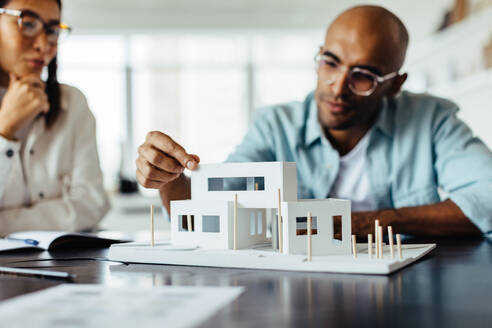 Architekt bespricht sein 3D-Hausmodell mit einem Kollegen, während er in einem Büro sitzt. Junge Geschäftsleute arbeiten an einem neuen Bauprojekt. - JLPSF28694