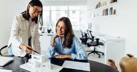 Two female architects discussing a 3D house model in an office. Creative business women collaborating on a new design project. - JLPSF28699