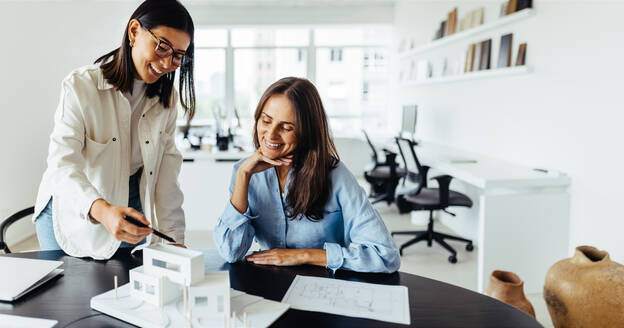 Zwei Architektinnen besprechen in einem Büro ein 3D-Hausmodell. Kreative Geschäftsfrauen arbeiten gemeinsam an einem neuen Designprojekt. - JLPSF28699