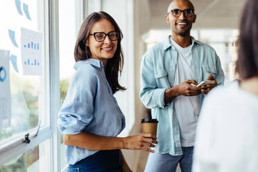 Business woman standing next to a window and having a meeting with her colleagues. Female sales executive working with her team in an office. - JLPSF28712