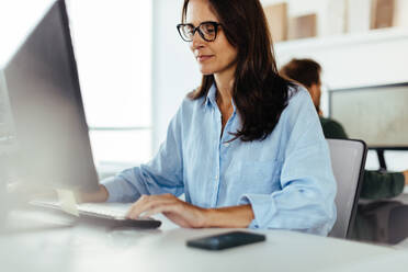 Eine Softwareentwicklerin arbeitet an einem Computer in einem Büro. Eine kreative Geschäftsfrau arbeitet an einem neuen Code, während sie an ihrem Schreibtisch sitzt. - JLPSF28717