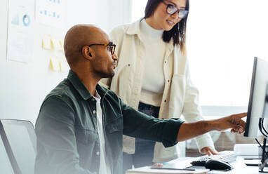 Software developer using a computer and having a discussion with his manager. Two creative business people working on a new coding project in an office. - JLPSF28719