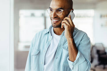 Black business man making a phone call while standing in his workplace. Male entrepreneur speaking to his business associates over the phone in an office. - JLPSF28750