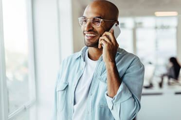 Junger Geschäftsmann, der an seinem Arbeitsplatz mit einem Mobiltelefon telefoniert. Männlicher Unternehmer, der in einem Büro telefoniert. - JLPSF28751