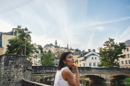 Weibliche Touristin, die auf einer Brücke in der Luxemburger Altstadt steht und die Aussicht genießt. Eine Frau beim Sightseeing in einer schönen Stadt. Dieses Foto hat absichtlich eine 35-mm-Filmkörnung verwendet. - JLPPF01561