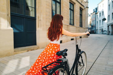 Weibliche Reisende, die eine Stadt mit dem Fahrrad erkundet. Eine Frau auf Sightseeing-Tour während eines Sommerurlaubs in Europa. Dieses Foto hat absichtlich eine 35-mm-Filmkörnung verwendet. - JLPPF01568