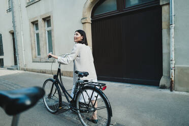 Weibliche Reisende, die mit dem Fahrrad neue Orte erkundet. Eine Frau, die im Urlaub eine europäische Stadt erkundet. Bei diesem Foto wurde absichtlich das Korn eines 35-mm-Films verwendet. - JLPPF01573