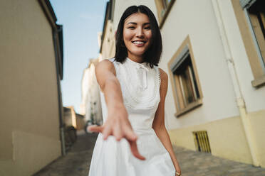 Junge Frau, die lächelt und die Kamera in einer Gasse blockiert. Eine Frau, die sich während eines Urlaubs in einer neuen Stadt amüsiert. Bei diesem Foto wurde absichtlich das Korn eines 35-mm-Films verwendet. - JLPPF01575