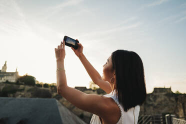 Weibliche Touristin, die auf einer Sightseeing-Reise in Europa die Aussicht fotografiert. Eine Frau, die im Urlaub landschaftliche Sehenswürdigkeiten erkundet. Bei diesem Foto wurde absichtlich eine 35-mm-Filmkörnung verwendet. - JLPPF01577