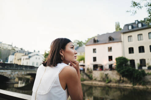 Frau auf einer Sightseeing-Tour in Europa. Weibliche Reisende betrachtet die Aussicht, während sie auf einer Brücke in Luxemburg steht. Dieses Foto hat absichtlich 35-mm-Filmkorn verwendet. - JLPPF01583