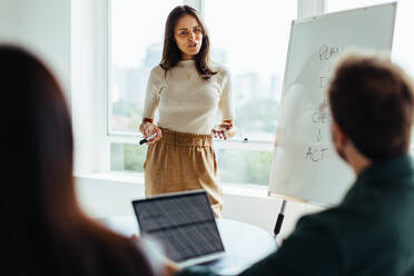 Eine Frau hält eine Präsentation in einem Büro. Eine reife Geschäftsfrau bespricht ihre Ideen mit ihrem Team während einer Besprechung. - JLPSF28761