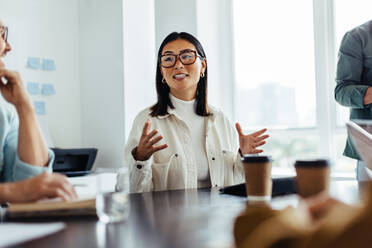 Business woman discussing a new project with her team in a meeting. Young woman explaining her business ideas while sitting in an office. - JLPSF28764