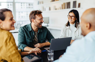 Verschiedene Geschäftsleute bei einer Teambesprechung in einem Büro. Eine Gruppe glücklicher Geschäftsleute, die um einen Tisch sitzen und eine Diskussion führen. - JLPSF28768