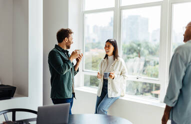 Happy business people chatting with each other during a coffee break in an office. Young business people working together in a casual office. - JLPSF28777