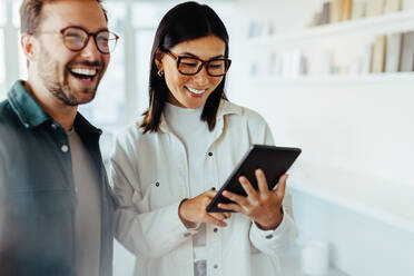 Female designer standing with her colleague and using a tablet. Happy business people working together in an office. - JLPSF28791