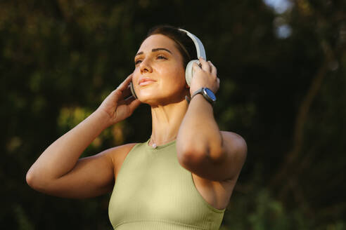 Fit woman listening to warmup music on headphones outdoors. Sportswoman preparing for a morning yoga workout. Exercising and practicing a healthy lifestyle. - JLPSF28826