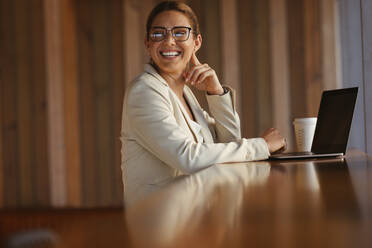 Happy business woman looking away while sitting with a laptop. Professional woman doing remote work in a coworking space. - JLPSF28842