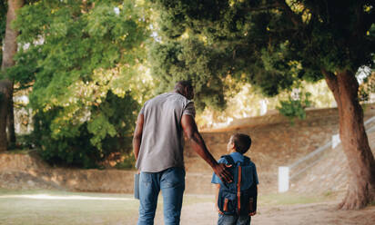 Child mentorship in primary school. Rearview of a male teacher talking and walking with a young school kid outside. Providing support and encouragement for a student in elementary school. - JLPSF28880