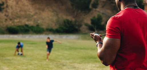 Ein Mann trainiert Schulkinder auf einem Sportplatz. Ein Fitnesstrainer macht eine Aufwärmübung mit einer Gruppe von Grundschulkindern. Sportunterricht in der Schule. - JLPSF28899