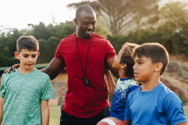 Zufriedener Trainer mit seiner Rugbymannschaft der Grundschule. Sportlehrer, der eine Gruppe von Kindern in der Grundschule trainiert. Betreuung und Förderung von Schülern. - JLPSF28905