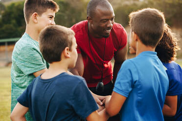 Sporttrainer bei einer Besprechung mit seiner Grundschulmannschaft. Lehrer bei einem motivierenden Gespräch mit seinen Schülern auf einem Feld. Mann, der eine Gruppe von Grundschulkindern betreut. - JLPSF28908